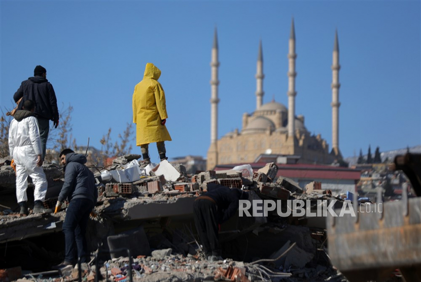  PBNU Imbau Sholat Ghaib dan Tahlil untuk Korban Gempa Turki dan Suriah. Foto: Orang-orang berdiri di atas puing-puing bangunan yang runtuh di kota Kahramanmaras, tenggara Turki,Rabu (8/2/2023). Lebih dari 11.000 orang tewas dan ribuan lainnya luka-luka setelah dua gempa besar melanda Turki selatan dan Suriah utara pada Senin (6/2/2023). Pihak berwenang khawatir jumlah korban tewas akan terus bertambah dan tim penyelamat terus mencari korban di seluruh wilayah.