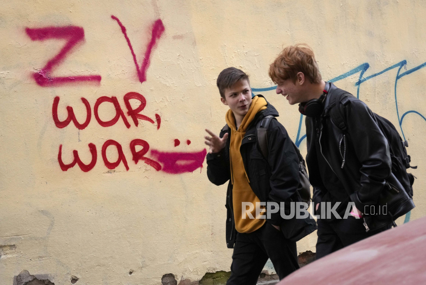 Pemuda berjalan melewati grafiti di dinding di St Petersburg, Rusia, Rabu, 23 Maret 2022. Huruf Z dan V, menjadi simbol militer Rusia.