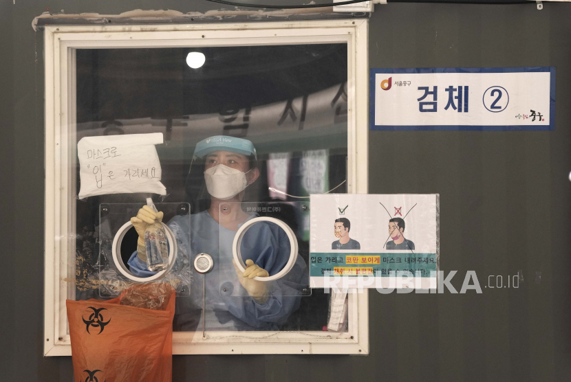 Seorang pekerja medis di bilik pengujian virus corona menyemprotkan disinfektan saat menunggu orang datang untuk tes di Seoul, Korea Selatan, Rabu, 4 Agustus 2021. Tanda di sebelah kiri berbunyi