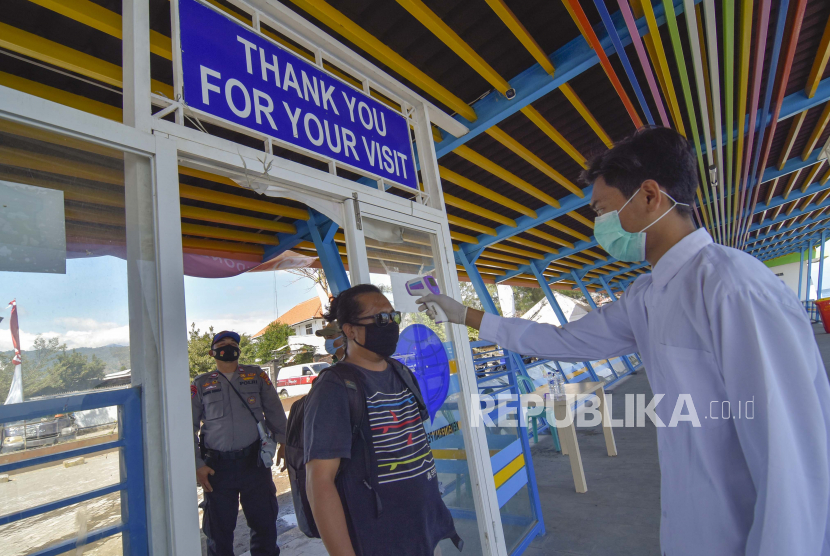 Petugas mengukur suhu tubuh pengunjung sebelum berangkat menuju Gili Trawangan di Pelabuhan Bangsal di Kecamatan Pemenang, Lombok Utara, NTB, Rabu (5/8). Presiden Joko Widodo (Jokowi) akhirnya merilis landasan hukum untuk penerapan sanksi bagi pelanggar protokol kesehatan. 