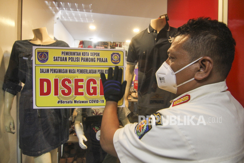 Petugas menempelkan stiker disegel sementara toko pakaian yang masih buka saat PSBB di salah satu pusat perbelanjaan.