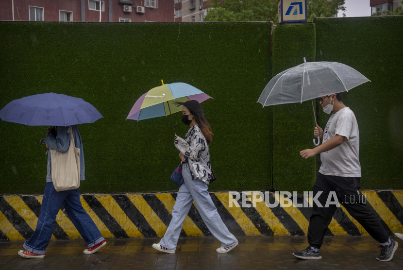  Komuter yang mengenakan masker berjalan di sepanjang jalan pada pagi yang hujan di Beijing, Jumat, 6 Mei 2022.