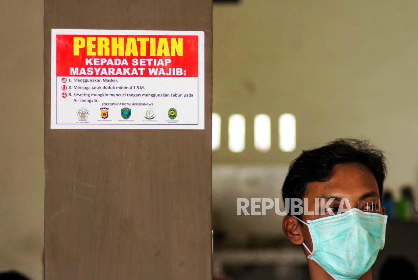 Warga berdiri disamping stiker sosialisasi pencegahan penyebaran Covid-19 yang ditempel di sebuah warung kopi di Lhokseumawe, Aceh, Senin (13/4/2020). Warga Aceh diserukan untuk tidak meremehkan risiko infeksi virus corona.