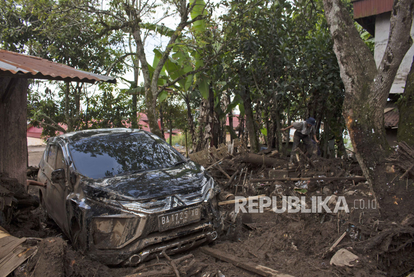 A man makes his way among the rubble near the wreckage of a car at a village affected by a flash flood in Agam, West Sumatra, Indonesia, Monday, May 13, 2024. Rescuers recovered more bodies Monday after monsoon rains triggered flash floods on Indonesia