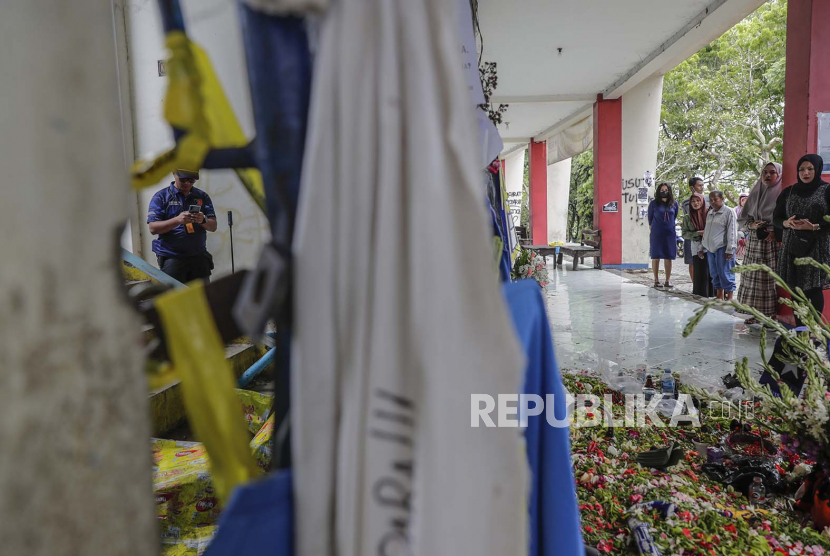 Seorang petugas polisi forensik menyelidiki di dekat pintu masuk tribun 13, lokasi utama penyerbuan, saat kerabat menyampaikan belasungkawa kepada para korban di Stadion Kanjuruhan di Malang, Jawa Timur, Indonesia, 06 Oktober 2022. Presiden Indonesia telah memerintahkan penyelidikan dan audit ke seluruh stadion sepak bola di tanah air, untuk memastikan keamanan bagi para penggemar setelah setidaknya 131 orang tewas dalam kerusuhan dan penyerbuan menyusul pertandingan sepak bola antara Arema FC dan Persebaya Surabaya di Jawa Timur pada 01 Oktober 2022.