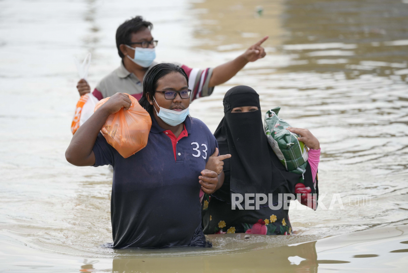 Warga mengarungi jalan yang banjir dengan membawa perbekalan mereka di Shah Alam, di pinggiran Kuala Lumpur, Malaysia, Senin, 20 Desember 2021.