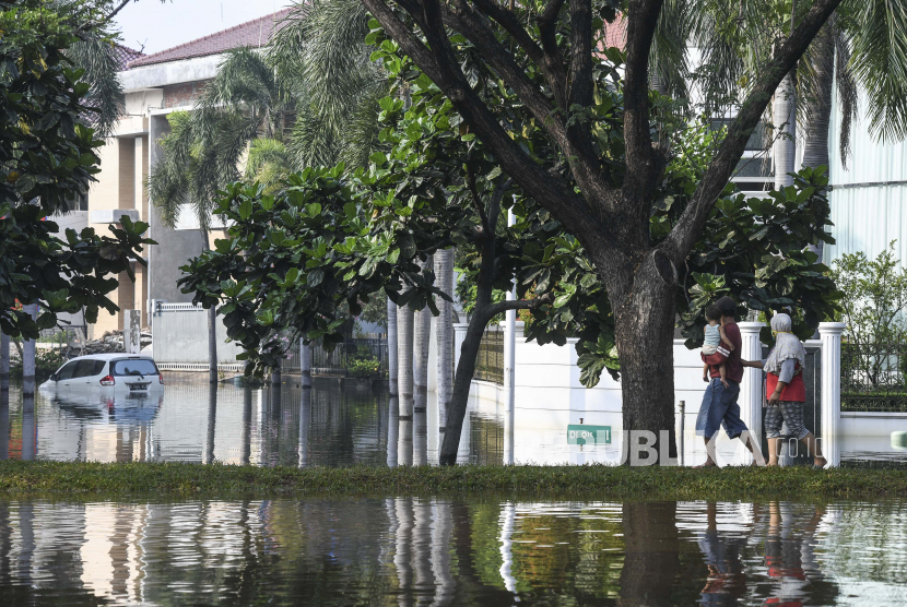 Warga melintas di Kompleks Pantai Mutiara yang tergenang banjir rob di Penjaringan, Jakarta, Ahad (7/6/2020). Banjir di kawasan tersebut diduga akibat adanya tanggul yang jebol saat naiknya permukaan air laut di pesisir utara Jakarta