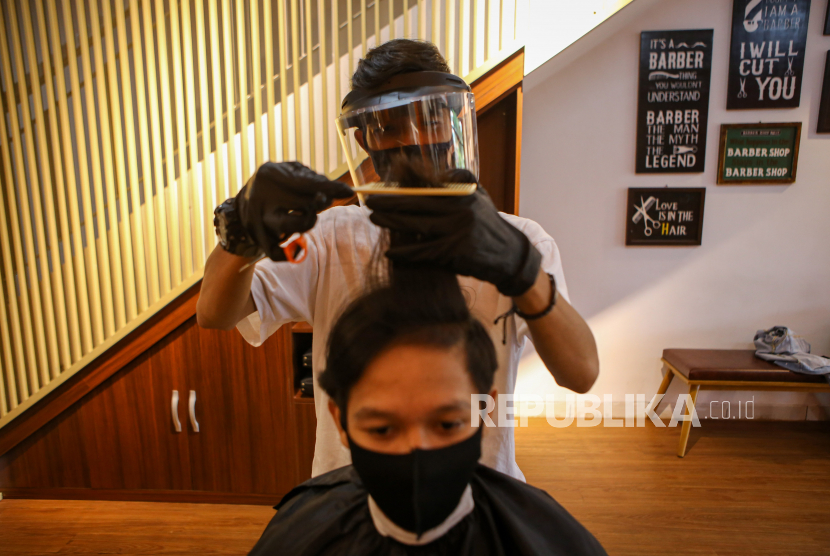 Pegawai yang mengenakan alat pelindung diri memotong rambut pelanggan di Crew Cuts and Space, Kota Tangerang, Banten, Ahad (5/7/2020). Banten resmi rilis Pergub Penerapan Disiplin dan Penegakan Hukum Protokol Kesehatan. Ilustrasi. 