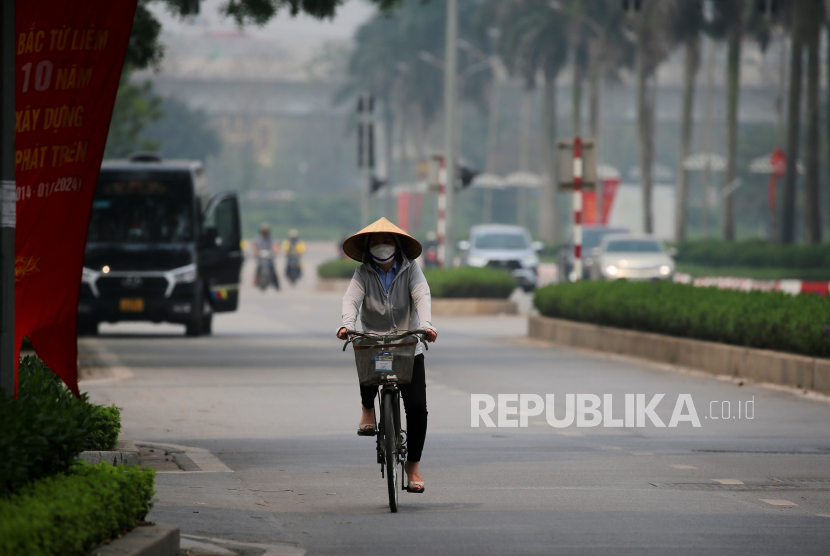 Seorang wanita yang mengenakan masker mengendarai sepeda di sepanjang jalan di Hanoi, Vietnam, 1 April 2024. 