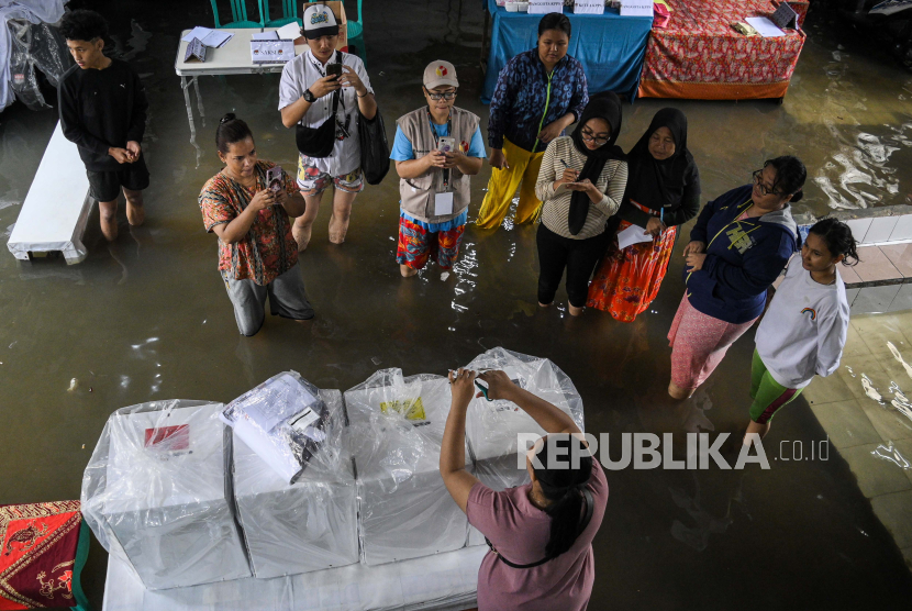 Sejumlah petugas menyiapkan Tempat Pemungutan Suara (TPS) 038 yang terendam banjir di Duri Kepa, Kebon Jeruk, Jakarta, Rabu (14/2/2024). Banjir setinggi 50 centimeter akibat intensitas hujan tinggi dan luapan Kali Sekretaris tersebut menyebabkan pelaksanaan pencoblosan sempat tertunda di TPS 039 dengan 271 Daftar Pemilih Tetap (DPT) dan TPS 038 dengan 268 DPT. 