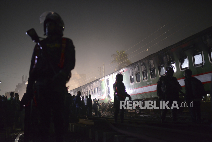 Petugas keamanan berdiri di dekat kereta penumpang yang terbakar di Gopibagh di Dhaka, Bangladesh, Jumat, (5/1/2024).