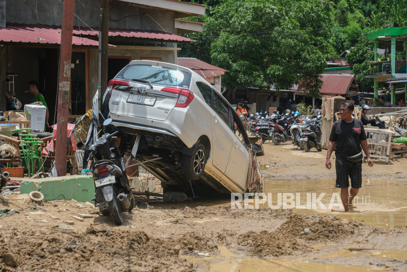 Warga melintas disamping mobil yang terseret saat banjir bandang akibat luapan Kali Lasolo di Kelurahan Sanua, Kendari, Sulawesi Tenggara, Kamis (7/3/2024). Kelurahan Sanua menjadi lokasi banjir bandang terparah dengan jumlah jiwa terdampak sekitar 42 ribu jiwa dan belum mendapatkan bantuan air bersih. 
