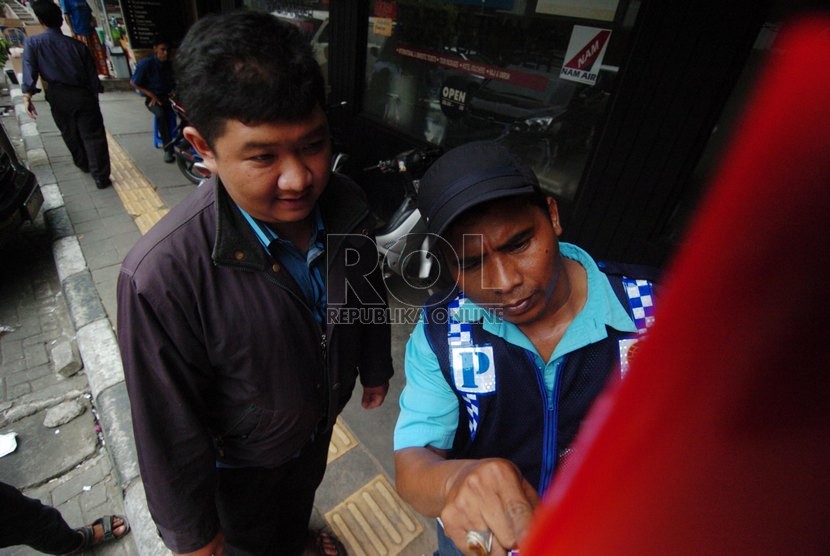   Pengendara dibantu juru parkir melakukan transaksi parkir dengan menggunakan mesin parkir meter di Jalan Sabang, Jakarta Pusat, Senin (6/10). (Republika/Raisan Al Farisi)