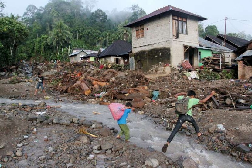   Dua orang anak menyeberang diantara tumpukan material yang terbawa arus banjir banjir bandang di Jorong Lungguk Nagari Koto Kaciak, Kecamatan Bonjol, Kabupaten Pasaman, Sumatera Barat, Ahad (16/11).  (Antara/Muhammad Arif Pribadi)
