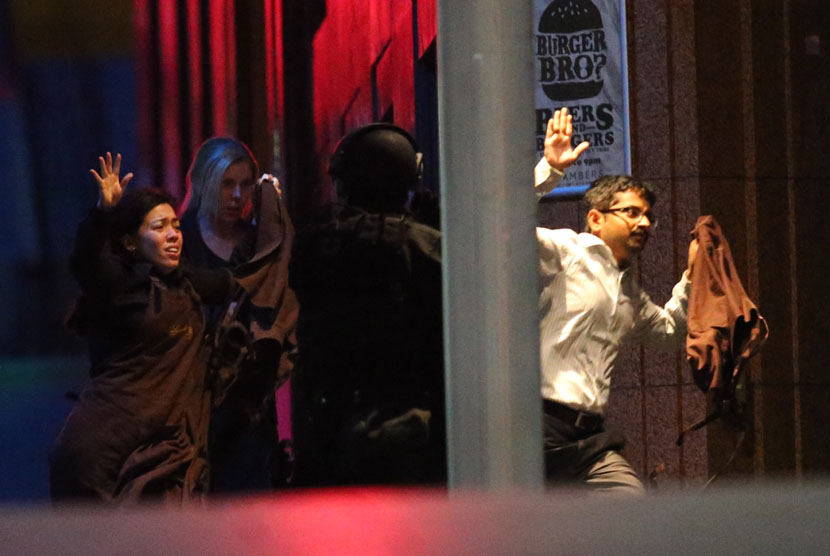  Seorang polisi bersenjata lengkap mengamankan sejumlah warga yang berhasil melarikan diri dari penyanderaan di sebuah kafe di Sydney, Senin (15/12). (AP/Rob Griffith)