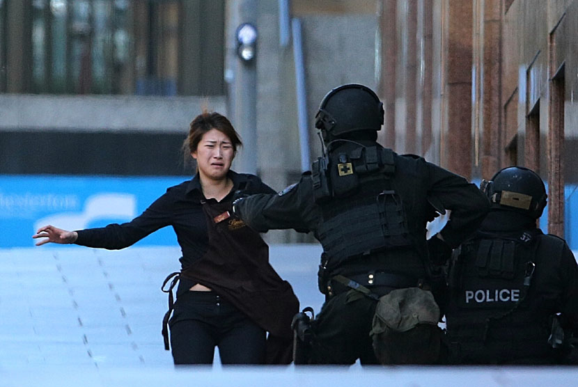  Sejumlah polisi bersenjata lengkap mengamankan seorang wanita yang berhasil melarikan diri dari penyanderaan di sebuah kafe di Sydney, Senin (15/12). (AP/Rob Griffith)
