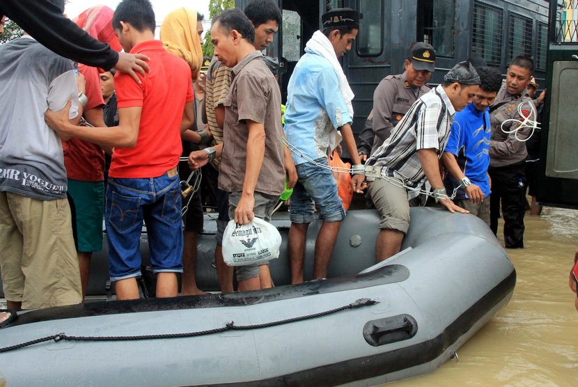 Polisi mengawal sejumlah narapidana turun dari perahu karet ketika melakukan evakuasi akibat lapas tempat mereka dibina terendam banjir di Lhoksukon, Aceh Utara, Aceh, Selasa (23/12). (Antara/Rahmad)