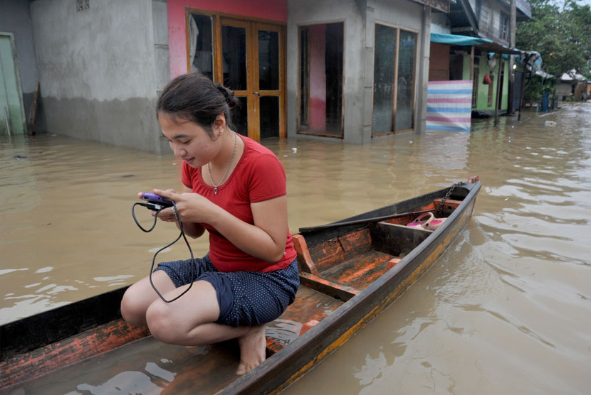   Seorang warga menggunakan ponsel saat berperahu di daerah  banjir di Desa Balai Karangan, Kecamatan Sekayam, Kabupaten Sanggau, Kalbar, Senin (19/1). (Antara/Jessica Helena Wuysang)