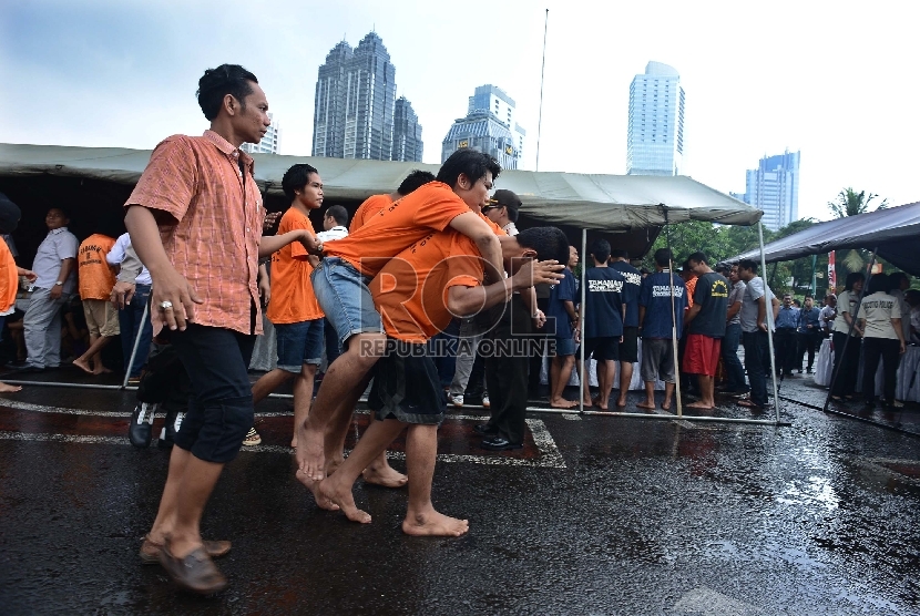  Seorang tahanan menggendong rekannya yang terkena tembak di kaki saat rilis operasi bina kusuma di Lapangan Parkir Ditlantas Polda Metro Jaya, Selasa (3/2). (Republika/Raisan Al Farisi)