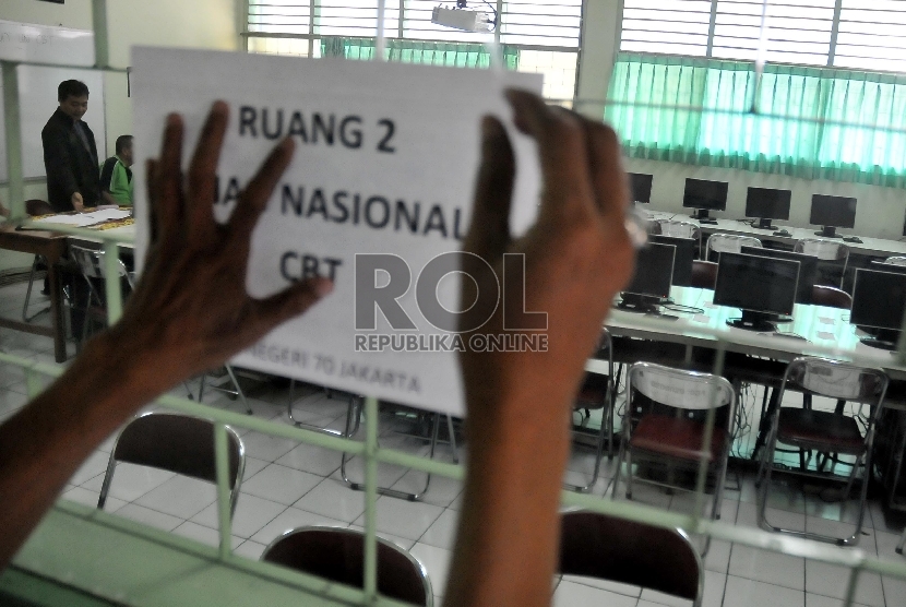 Petugas memasang informasi ruang ujian saat proktor melakukan singkronisasi soal dari server pusat ke server sekolah untuk Ujian Nasional (UN) di SMA 70 Jakarta, Ahad (12/4).  (Republika/Rakhmawaty La'lang)