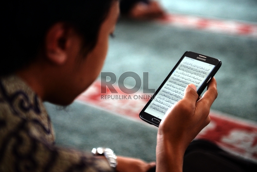 Seorang jamaah membaca ayat Alquran melalui smartphone.