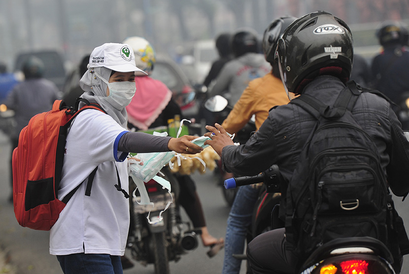   Seorang petugas dari Dinas Kesehatan Pemprov Jambi membagikan masker gratis kepada pengendara yang melintasi  Jalan A. Rahman Saleh, Jambi, Rabu (9/9).  (Antara/Wahyu Putro A)