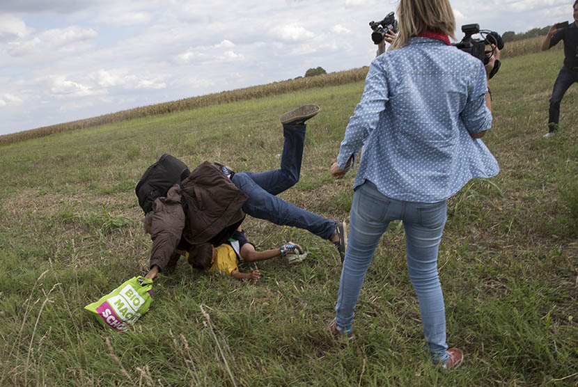  Seorang imigran yang menggendong anaknya terjatuh seteah ditendang oleh pewarta video Petra Laszlo (kanan) di Desa Roszke, Hungaria, Rabu (9/9).  (Reuters/Marko Djurica)