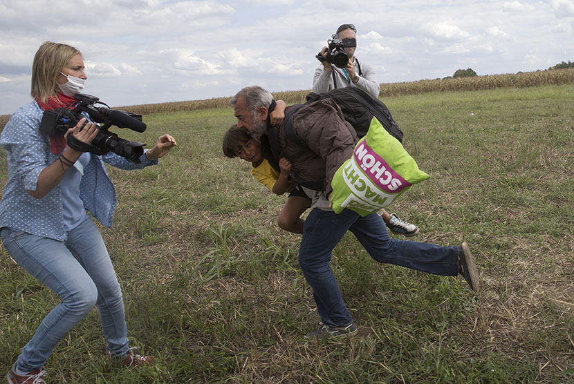  Seorang imigran yang menggendong anaknya berusaha melarikan diri , sebelum terjatuh ditendang oleh pewarta video Petra Laszlo (kiri) di Desa Roszke, Hungaria, Rabu (9/9).  (Reuters/Marko Djurica)