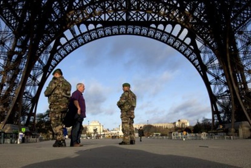  Warga berbincang dengan tentara yang berpatroli di Menara Eiffel yang ditutup pada hari pertama berkabung nasional di Paris, Ahad (15/11).  (AP/Peter Dejong)