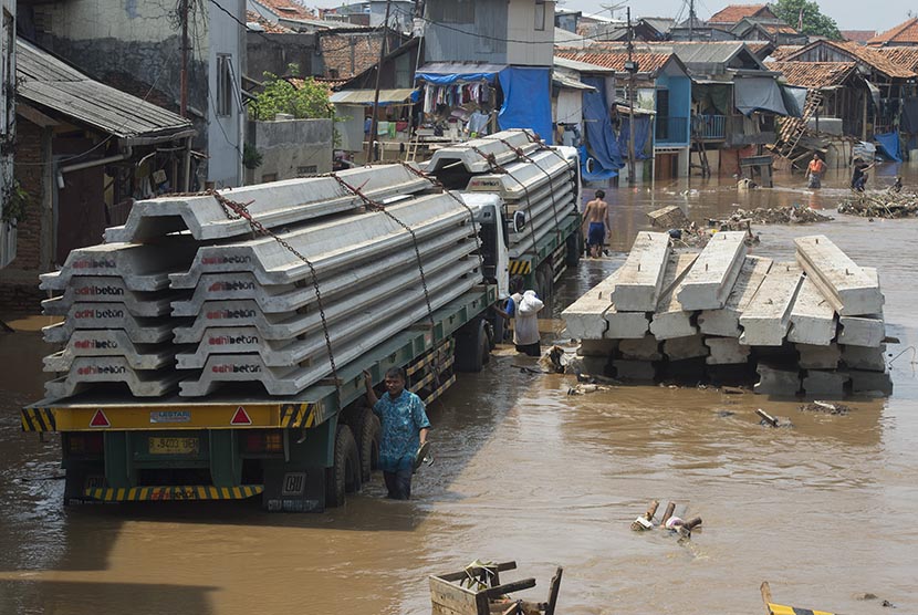 Warga melintas di samping dua buah truk pengangkut turap yang ikut terendam luapan air Sungai Ciliwung di kawasan proyek normalisasi, Kampung Pulo, Jatinegara, Jakarta Timur, Rabu (25/11).  (Antara/Widodo S. Jusuf)