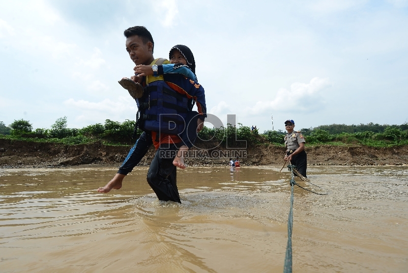   Satpolair Polres Purwakarta menggendong siswa Madrasah Ibtidaiyah untuk menyeberangi Sungai Cilalawi pulang dari sekolah menuju rumahnya di Kabupaten Purwakarta, Jumat (11/12). (Republika/Raisan Al Farisi)
