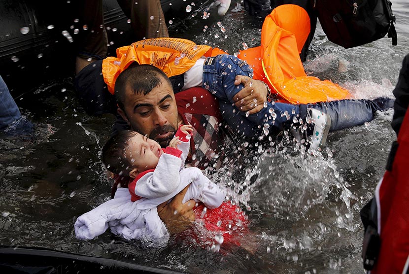  Seorang pria pengungsi Suriah memegang erat anaknya saat berusaha mencapai pantai Pulau Lesbos di Yunani.  (REUTERS/Yannis Behrakis)