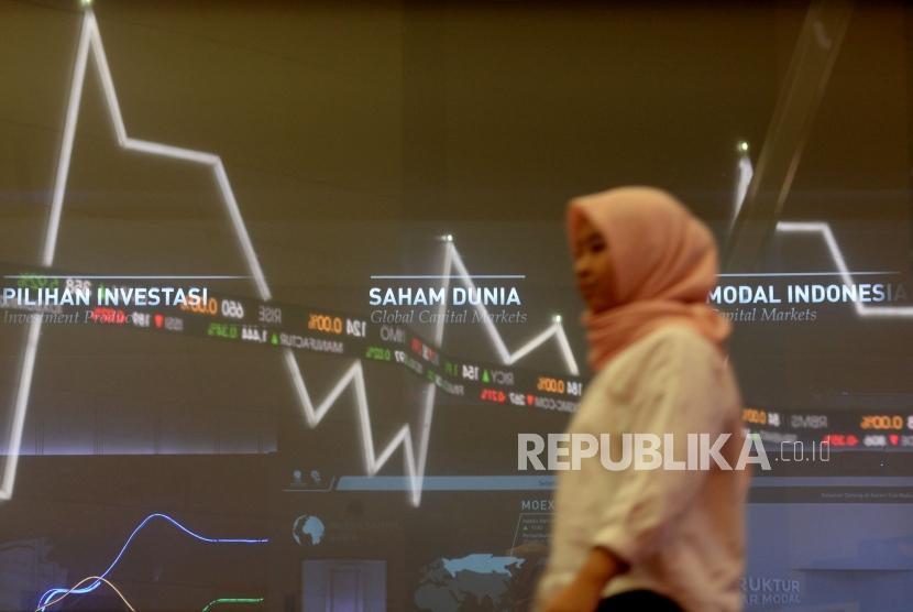 Karyawan melintas di dekat layar pergerakan saham di gedung Bursa Efek Indonesia, Jakarta,Senin (21/10).
