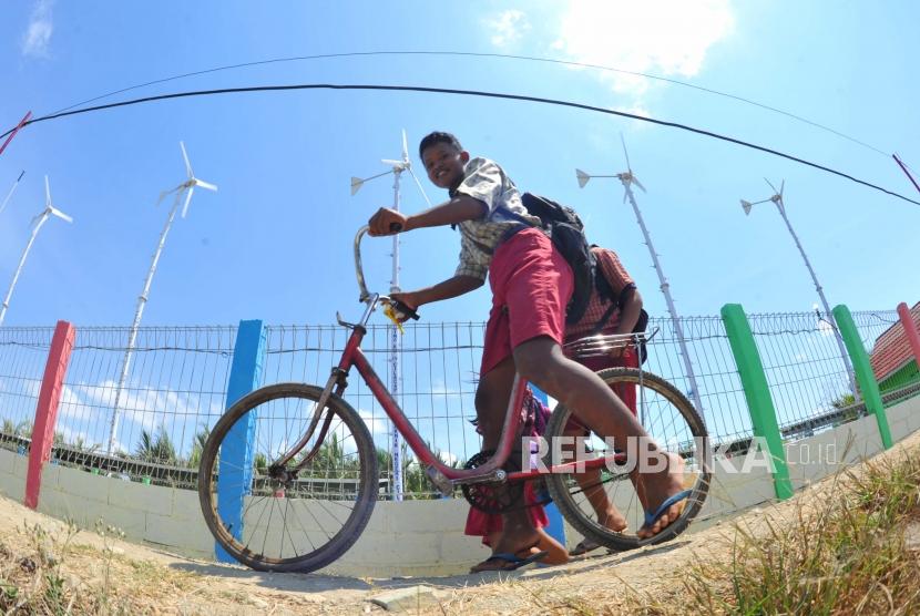 Pembangkit Listrik Tenaga HybridPelajar melintas berlatar kincir angin Energi Mandiri Tenaga Surya dan Angin ( E Mas Bayu), Kampug Laut, Cilacap, Jawa Tengah, Kamis (24/10).