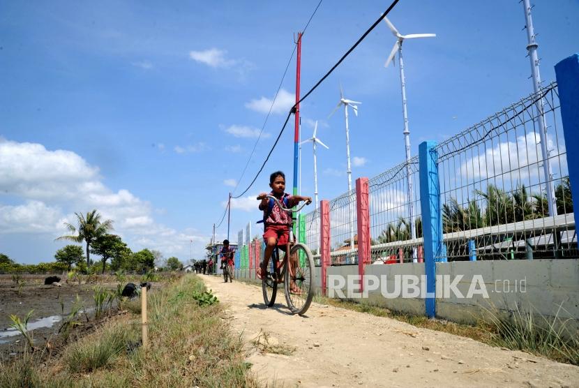 Pelajar melintas berlatar kincir angin Energi Mandiri Tenaga Surya dan Angin ( E Mas Bayu), Kampug Laut, Cilacap, Jawa Tengah (ilustasi). 