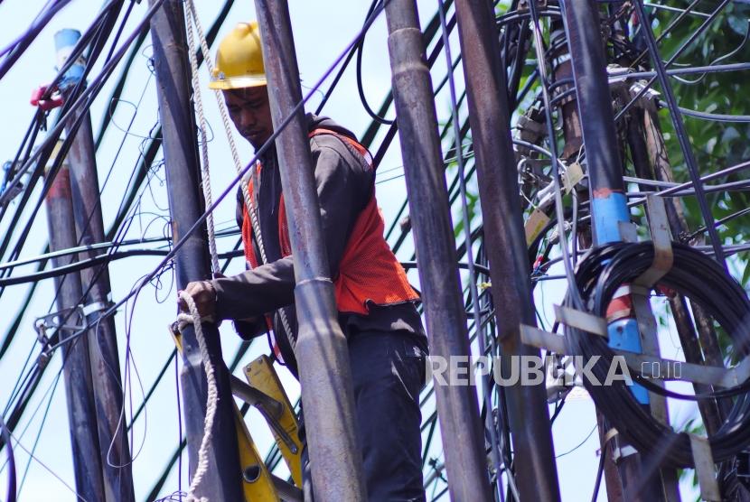 Seorang pekerja sedang mengikatkan tali katrol dalam upaya mencabut tiang kabel optik untuk dimasukkan ke dalam tanah di Jalan Raya Kemang, Jakarta Selatan, Senin (18/11/2022).
