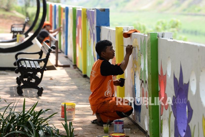 Petugas PPSU kelurahan Pondok Bambu membuat mural di tembok halte sepeda kawasan Banjir Kanal Timur (BKT), Jakarta, Rabu (20/11).