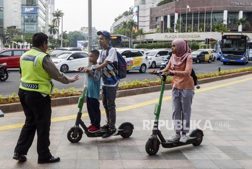 Anggota kepolisian menghentikan pengguna skuter listrik yang melintas di jalan MH Thamrin, Jakarta, Ahad (24/11).