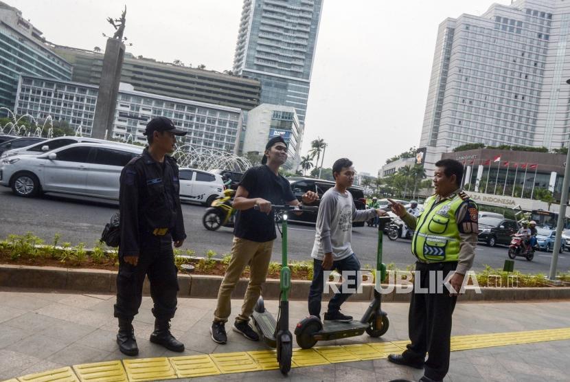Anggota kepolisian memberi himbauan kepada pengguna skuter listrik yang melintas di jalan MH Thamrin, Jakarta, Ahad (24/11).