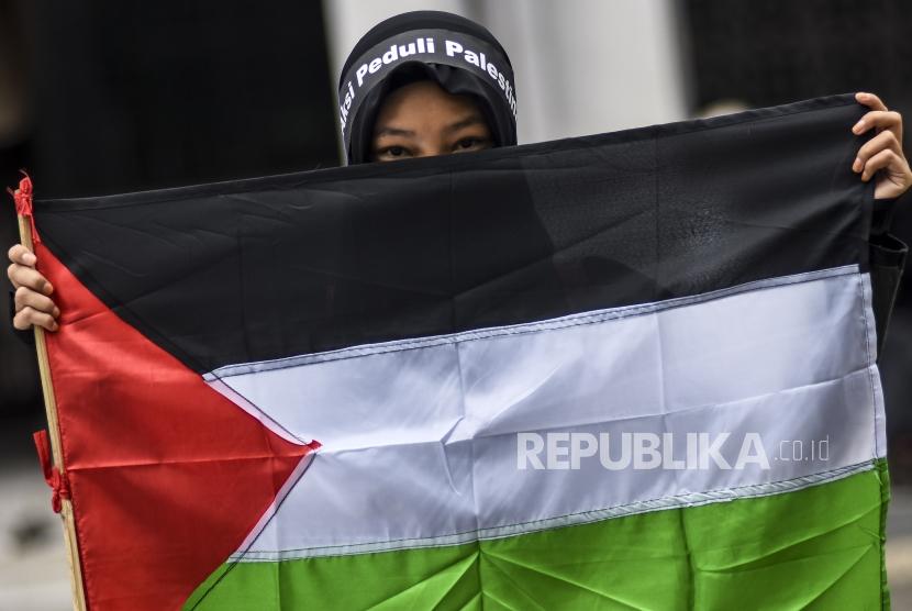 Seorang peserta aksi memegang bendera Palestina saat demonstrasi mengecam Israel di Kota Bandung.
