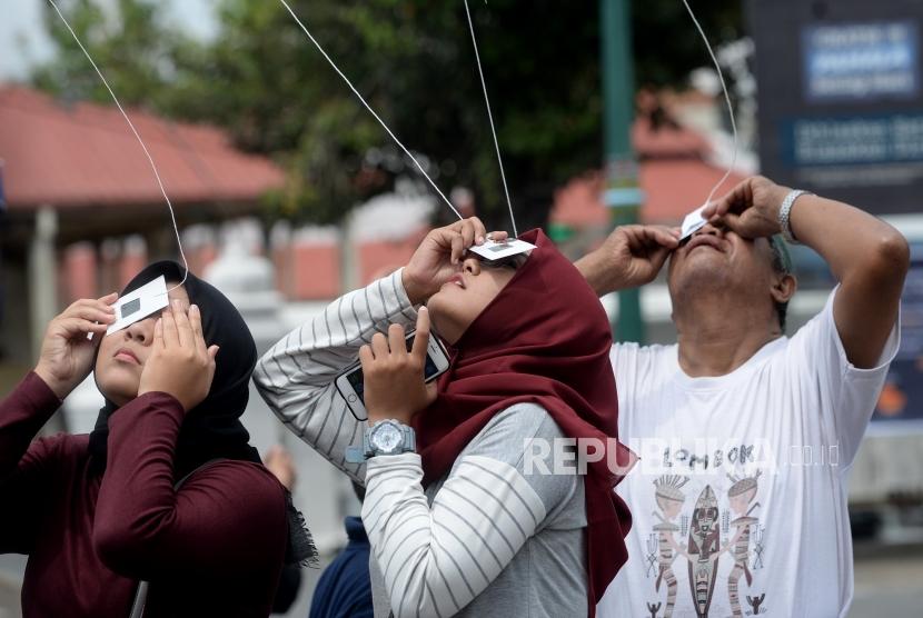 Melihat Gerhana Matahari Yogyakarta. Warga dan wisatawan mencoba megamati proses gerhana matahari dengan alat bantu di Halaman Masjid Gede, Yogyakarta, Kamis (26/12).