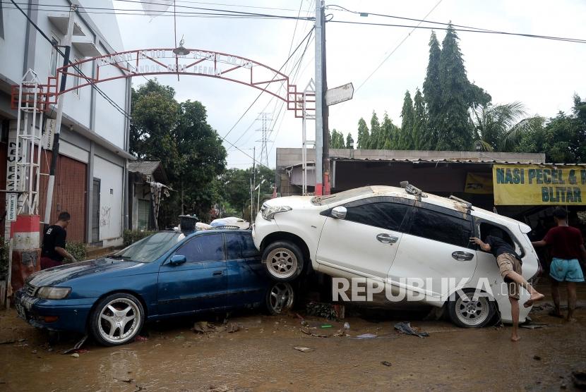 Sejumlah warga berjalan di dekat mobil yang rusak pascabanjir di Perumahan Pondok Gede Permai Bekasi, Jawa Barat, Kamis (2/1). Pemprov Jabar sudah menandatangani surat tanggap darurat untuk enam wilayah.