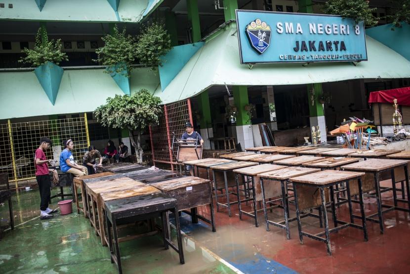 Guru dan murid membersihkan meja dan kursi pascabanjir yang merendam SMA Negeri 8 Jakarta di Bukit Duri, Tebet, Jakarta, Sabtu (4/1/2020).