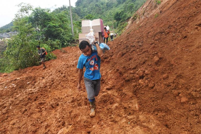 Warga korban longsor sambil membawa logistik menaiki bukit untuk menuju rumah mereka yang terdampak longsor di Sukajaya, Bogor, Jawa Barat, Minggu (5/1/2020).