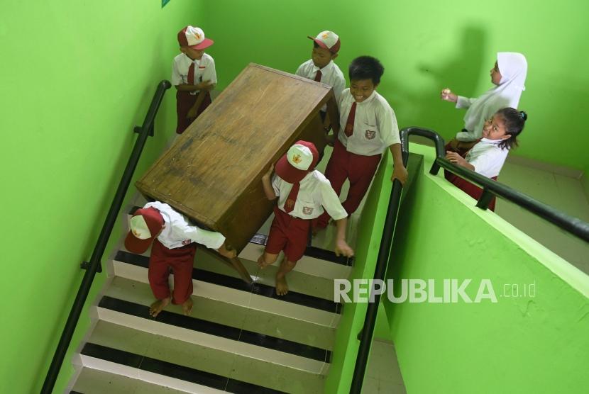 Siswa Sekolah Dasar Negeri Kapuk Muara 01 bergotong royong memindahkan meja, kursi dan lemari kedalam ruang kelas saa kerja bakti bersama pasca banjir di Jakarta, Senin (6/1/2019).