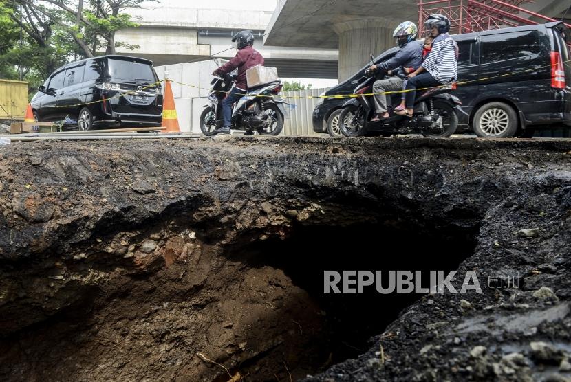 Pengendara motor melihat kondisi jalan yang ambles di Jalan Daan Mogot, Tangerang, Banten, Senin (13/1).