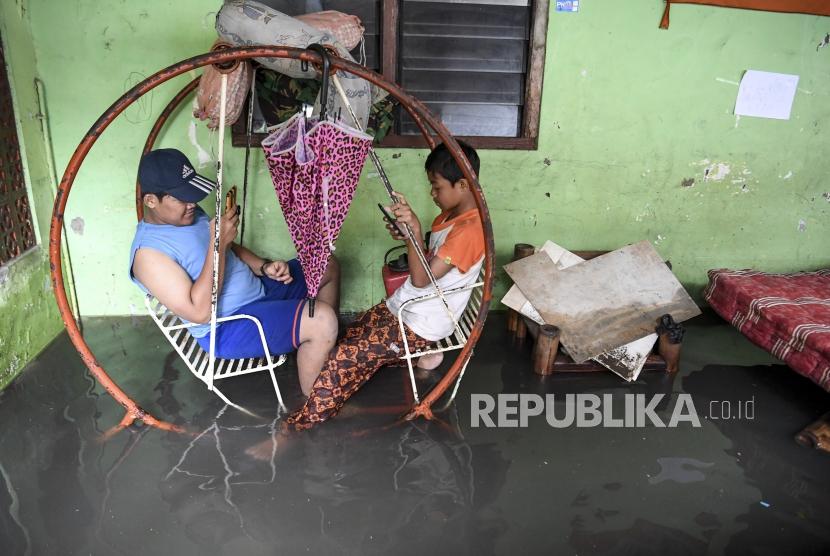 Dua orang anak bermain gawai di rumahnya yang terendam banjir  (ilustrasi)