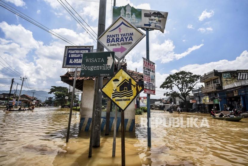 Sejumlah warga menggunakan perahu melintasi genangan banjir di ruas Jalan Raya Banjaran, Kecamatan Baleendah, Kabupaten Bandung, Ahad (26/11).