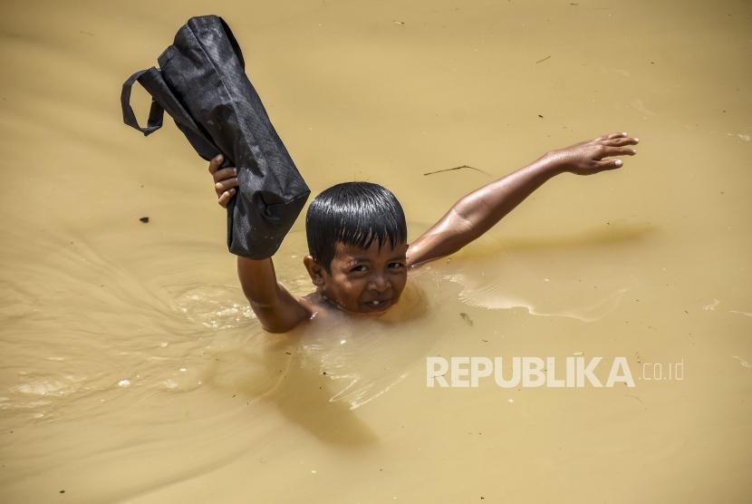 Seorang anak membawa tas melintasi genangan banjir di Jalan Katapang Andir, Kecamatan Baleendah, Kabupaten Bandung, Ahad (26/11).
