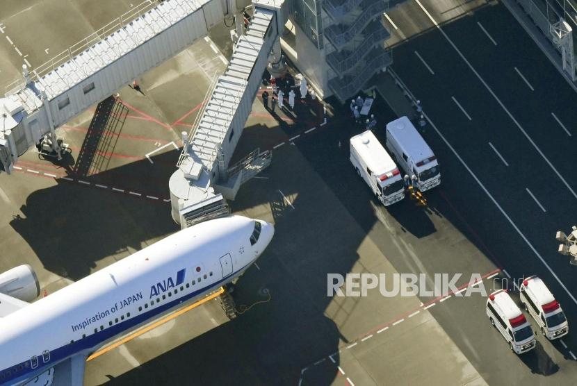 Petugas mengenakan pakaian pelindung berada di sekitar pesawat yang mendarat membawa warga Jepang dari Wuhan di Bandara Haneda, Tokyo, Jepang, Rabu (29/1).
